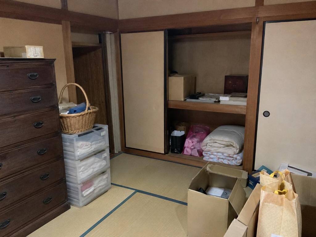 空き家売却前、押し入れの寝具や段ボール・古い箪笥など残った家財を確認している和室のイメージ